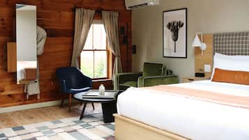 A hotel room with a wooden wall, a bed, a desk, a chair, a lamp, and a picture on the wall.