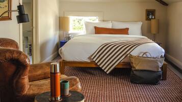 A bedroom with a large bed, a wooden headboard, a red and white patterned rug, and a leather armchair.