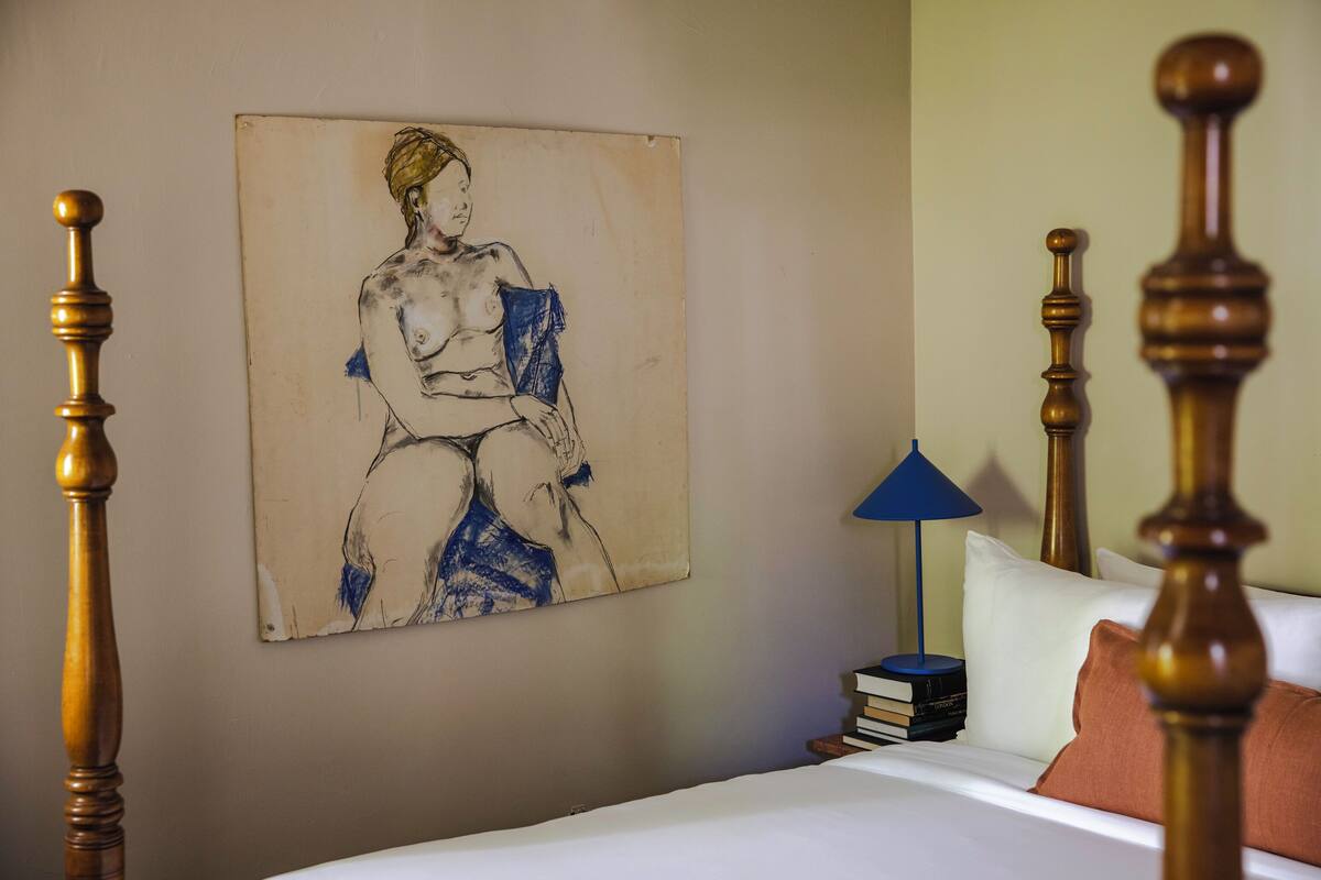 Een slaapkamer met een bed, een nachtkastje met boeken, een lamp en een schilderij aan de muur.