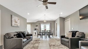 Ein geräumiges Wohnzimmer mit zwei Ledersofas, einem Esstisch und einem Deckenventilator.