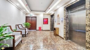 Un hall de hotel con piso de mármol, una recepción, un área de espera y un ascensor.