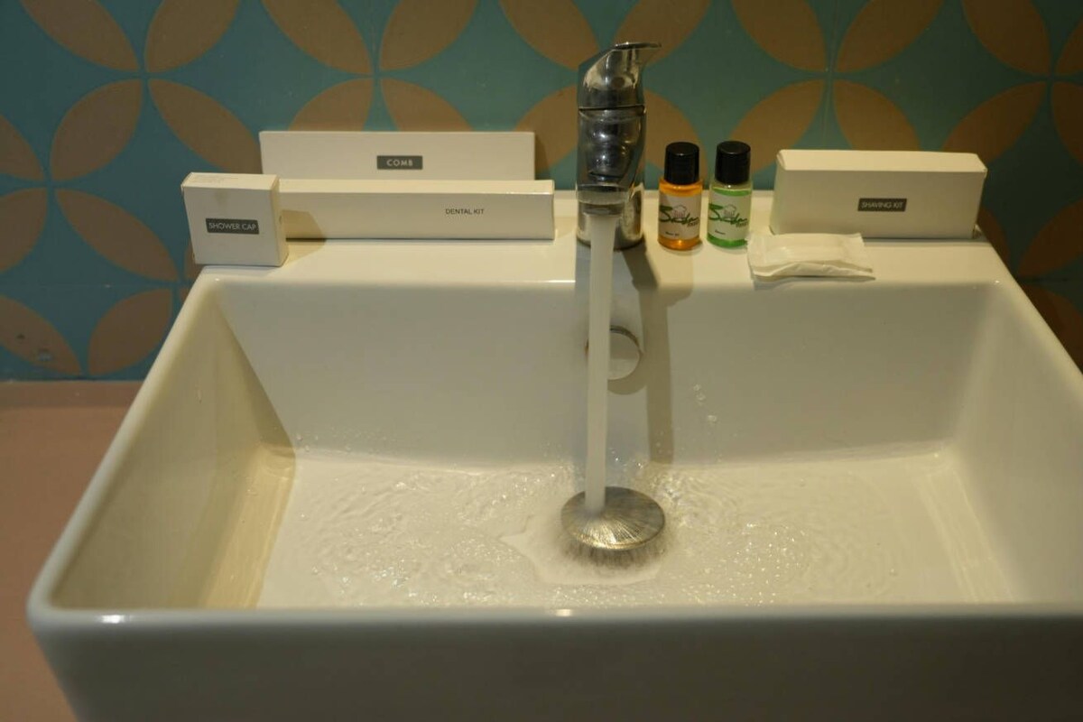 A bathroom sink with a shower head, a comb, a toothbrush, and a bottle of mouthwash.