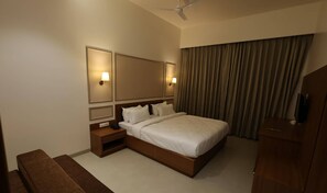 A hotel room with a large bed, nightstands, a mirror, and a ceiling fan. - Baba (Nandurbar)