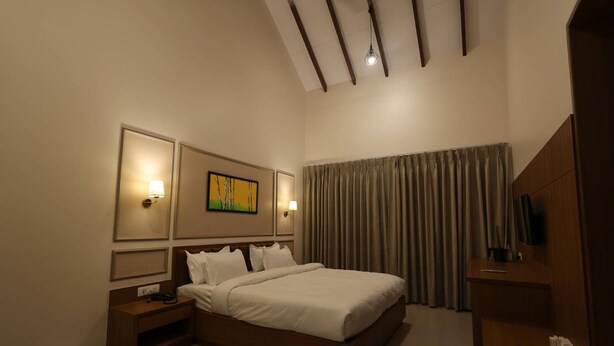 A hotel room with a bed, bedside tables, a TV, and a painting on the wall. - Baba (Nandurbar)