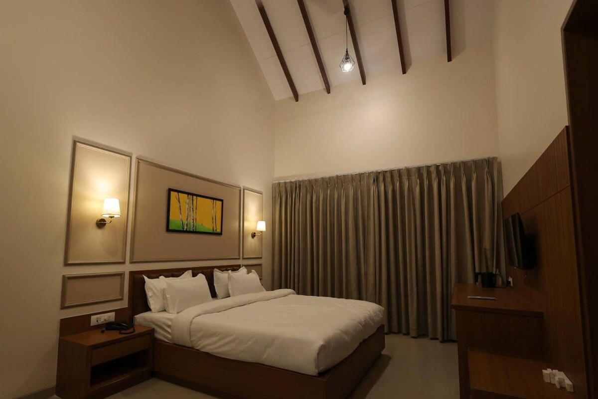 A hotel room with a large bed, a nightstand, a TV, and a painting on the wall.