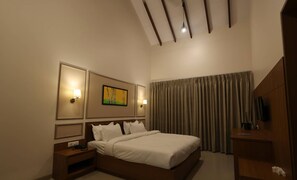 A hotel room with a large bed, a nightstand, a TV, and a painting on the wall. - Baba (Nandurbar)