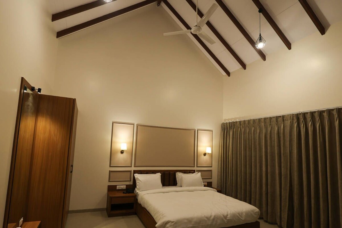 A hotel room with a bed, a wooden wardrobe, a ceiling fan, and a large mirror.