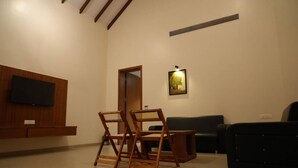 A living room with a flat-screen TV mounted on a wooden panel, a black sofa, and a wooden coffee table. - Baba (Nandurbar)