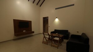 A living room with a flat-screen TV mounted on the wall, a dining table with chairs, a black sofa, and a black armchair. - Baba (Nandurbar)