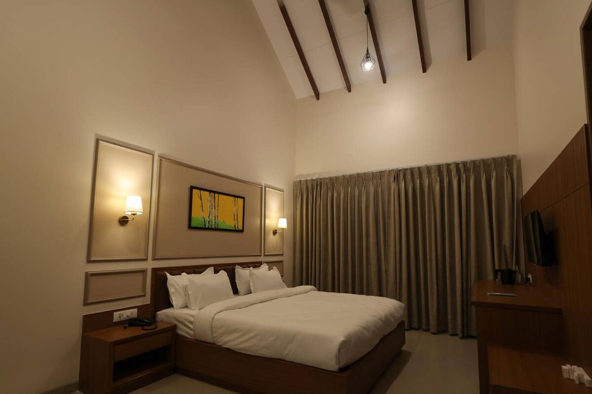 A hotel room with a bed, bedside tables, a TV, and a painting on the wall.
