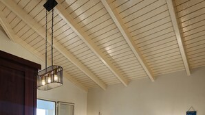 A bedroom with a wooden bed, two bedside tables with lamps, a nightstand, a chair, and a ceiling with wooden beams.