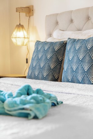 A bed with a white headboard, two patterned pillows, a blue blanket, and a wall-mounted lamp.
