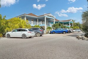 A two-story building with a balcony and a covered porch, surrounded by parked cars and palm trees. - Caribbean Lofts 24 - Waterfront (Kralendijk)