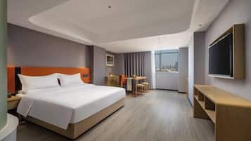 Una habitación de hotel moderna con una cama grande, un escritorio, una silla, un televisor y vistas a la ciudad.