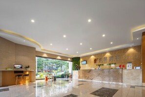 A hotel reception area with a marble reception desk, a TV, and a seating area with stools. - Parlor Hotel (Dongguan)