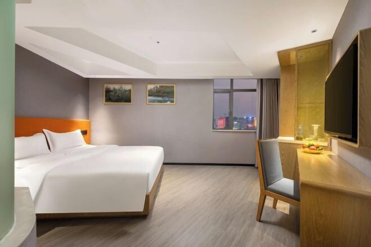 Habitación de hotel con cama, escritorio y silla, y un amplio ventanal con vistas a la ciudad.