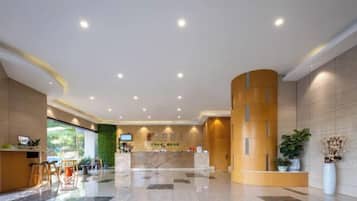 Un hall de hotel con mostrador de recepción, zona de estar y una planta grande.