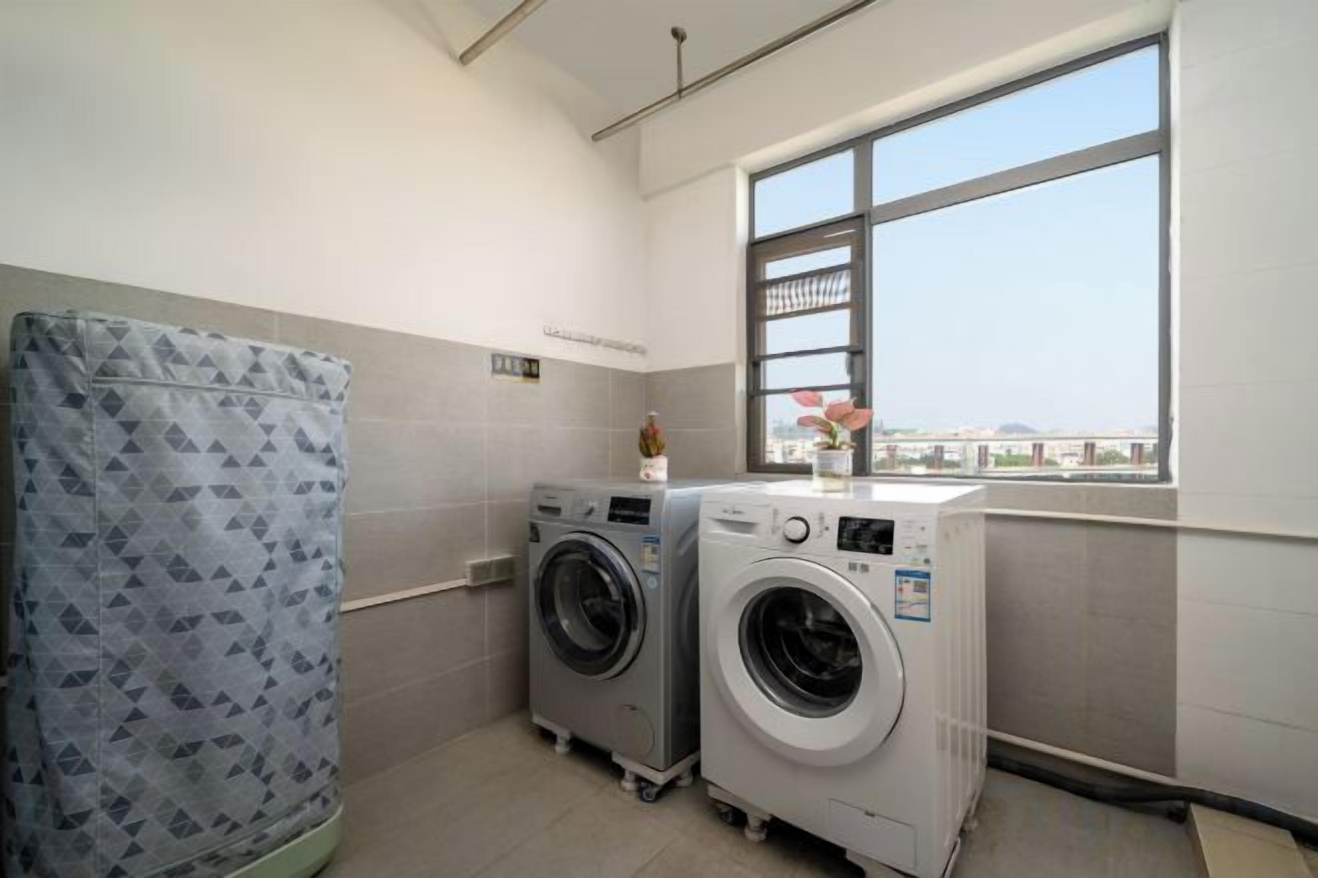 A laundry room with two washing machines, a drying machine, and a large window with a view.