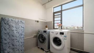 A laundry room with two washing machines, a drying machine, and a large window with a view.