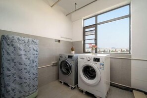 Une buanderie équipée de deux machines à laver, d’un sèche-linge et d’une grande fenêtre donnant sur un beau paysage.