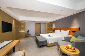 Una habitación de hotel moderna con una cama, un sofá, un televisor, una pequeña mesa con fruta y un banco.