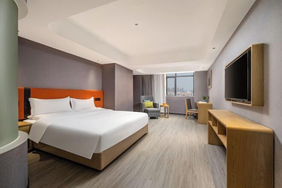 Habitación de hotel con una cama grande, un escritorio, una silla y un televisor fijado en la pared.