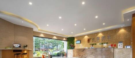 A hotel reception area with a marble counter, a television, and a seating area with stools.