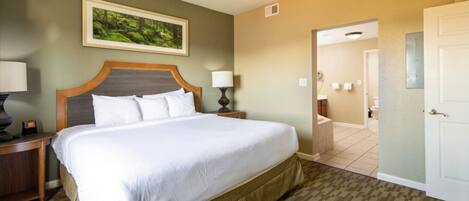 A hotel room with a large bed, a nightstand with a lamp, a framed picture on the wall, and a bathroom visible through an open door.