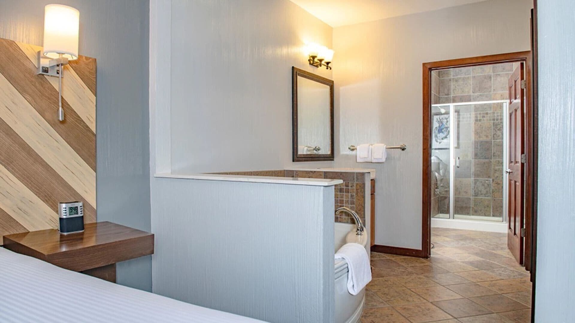 A modern bathroom with a wooden accent wall, a large mirror, a shower, and a clock on the counter.