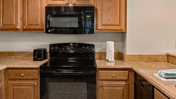 Una cocina con armarios de madera, un microondas negro, una estufa y un tostador.