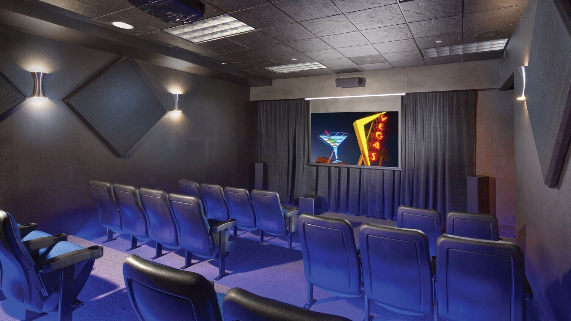 A movie theater with rows of seats, a screen, and a neon sign.