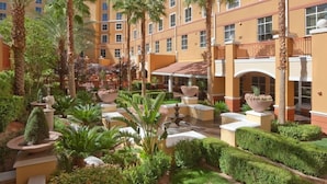 A courtyard with palm trees, a fountain, and a building with multiple windows.