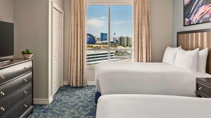 A hotel room with a large bed, a dresser, a television, and a view of a cityscape through the window.