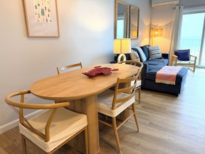 A dining area with a wooden table and chairs, a sofa, a lamp, and a framed picture on the wall.
