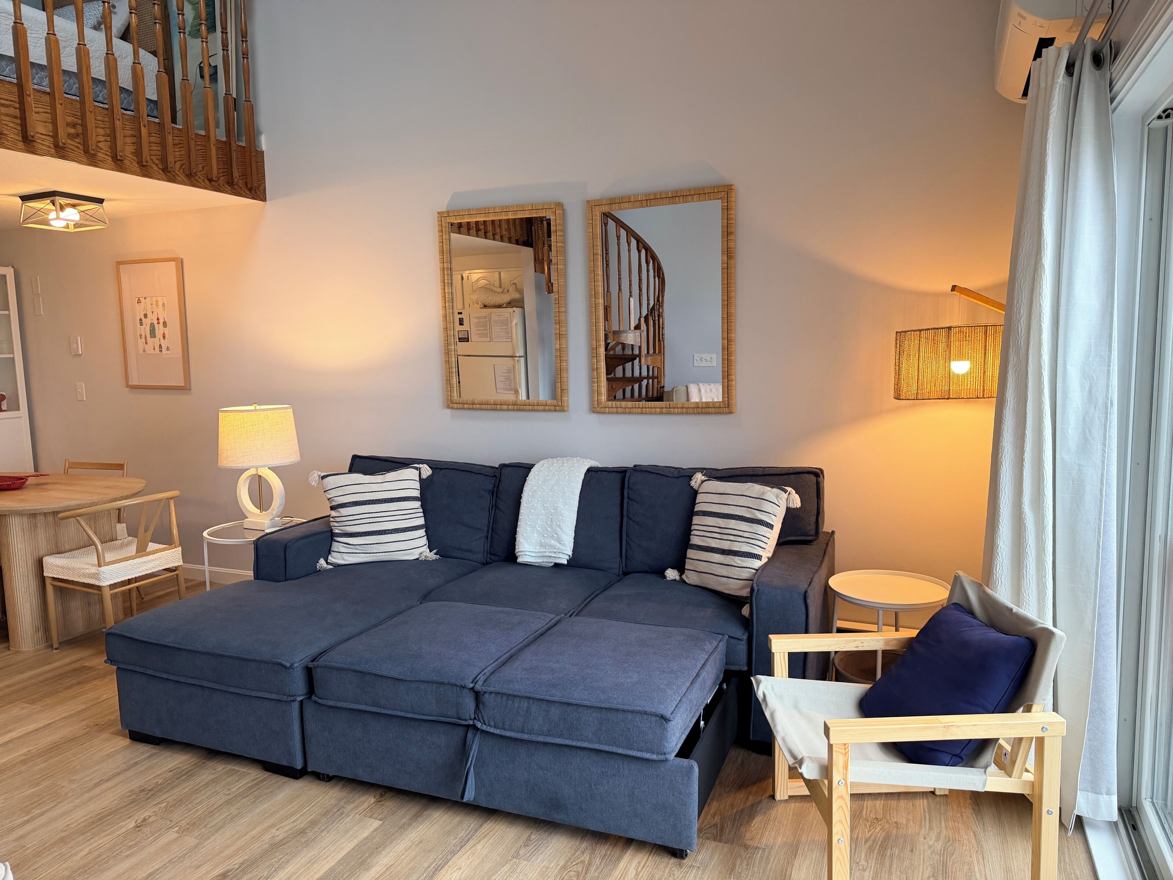 A modern living room with a sofa, a dining table, a lamp, and a staircase.