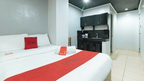 A hotel room with a bed, a red towel, a red pillow, a red bed runner, a black minibar, and a white door. - Reddoorz @ Good 101 Quiricada Manila (Manila)