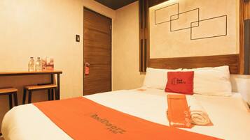 Una camera d'albergo con un letto rifatto, una scrivania con bottiglie d'acqua e un asciugamano con il marchio RedDoorz.