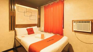 A hotel room with a bed, a red door sign, a window with blinds, and a wall-mounted air conditioning unit.