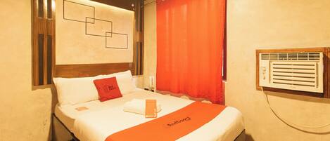 Quarto de hotel com cama, placa vermelha na porta, janela com persianas e ar condicionado fixado na parede.