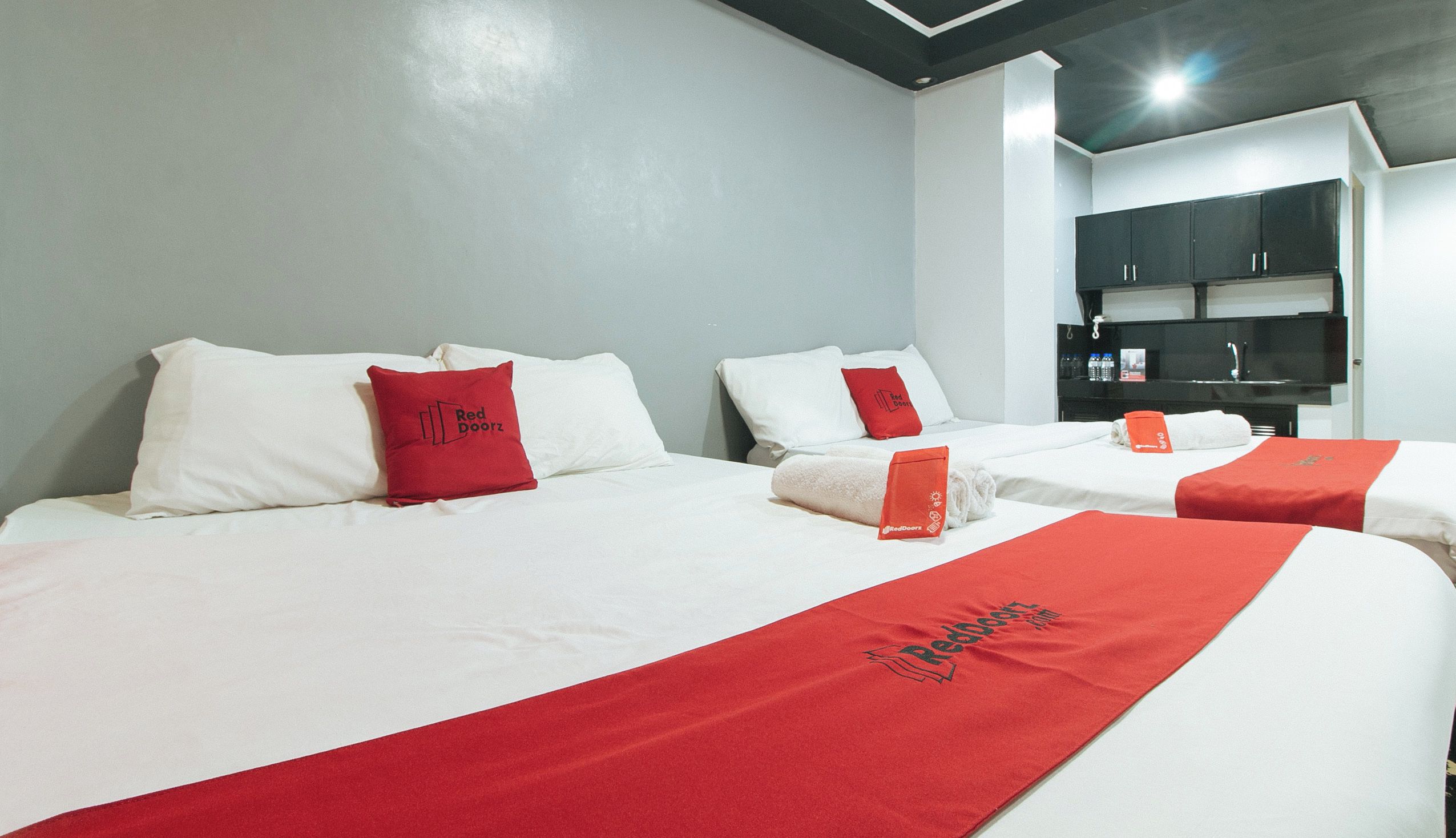 Een hotelkamer met twee bedden, elk voorzien van wit beddengoed en rode accenten, inclusief kussens en een rode handdoek. Er is een minibar en een televisie op een zwart kastje.