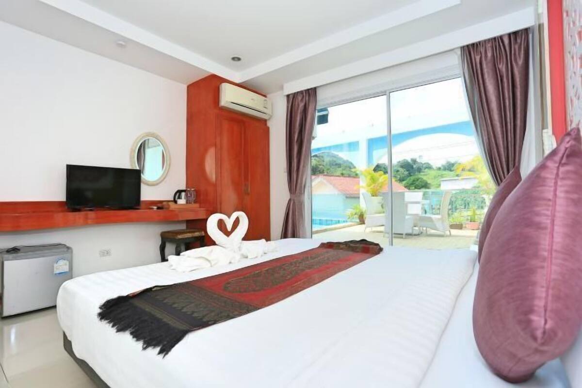 A hotel room with a bed, a television, an air conditioning unit, a small desk, and a window with curtains.