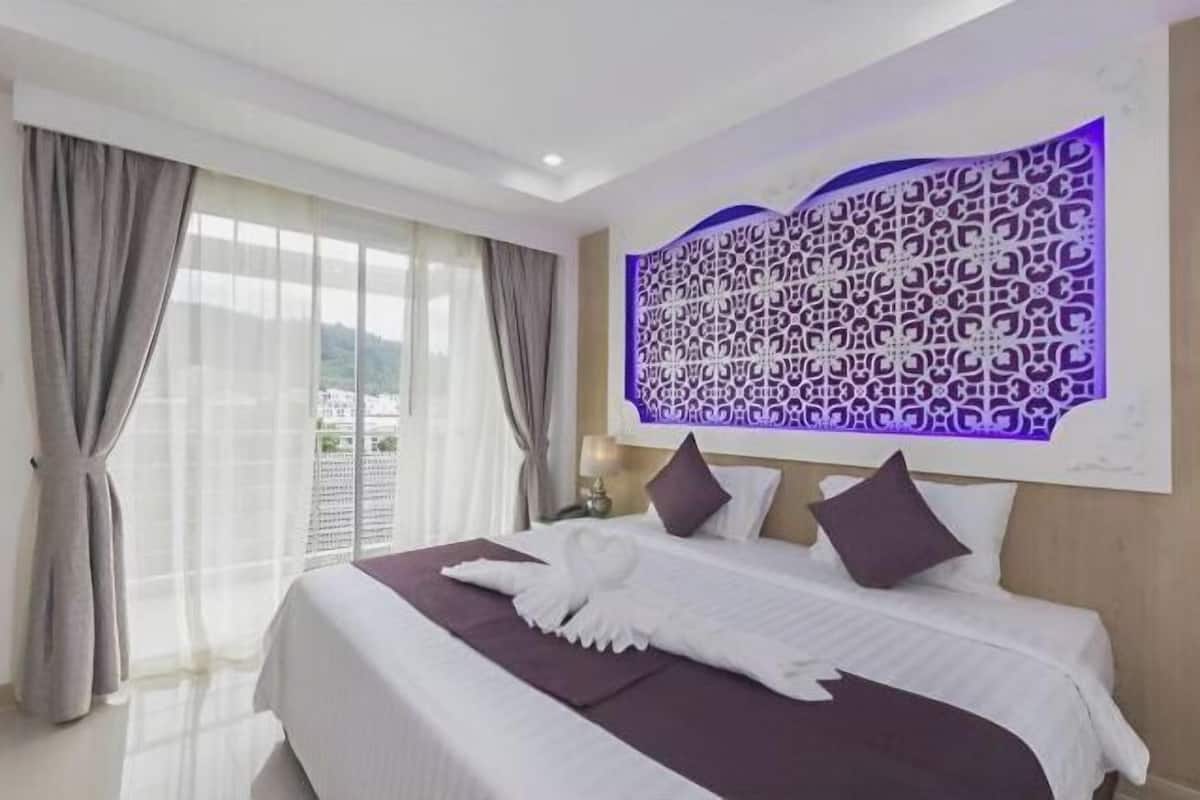 A hotel room with a large bed, a decorative wall panel, and a view through the window.