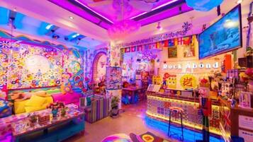 Um quarto vibrante e colorido, com um design divertido, que apresenta um sofá, uma mesa com vários objetos e um balcão com produtos à venda.