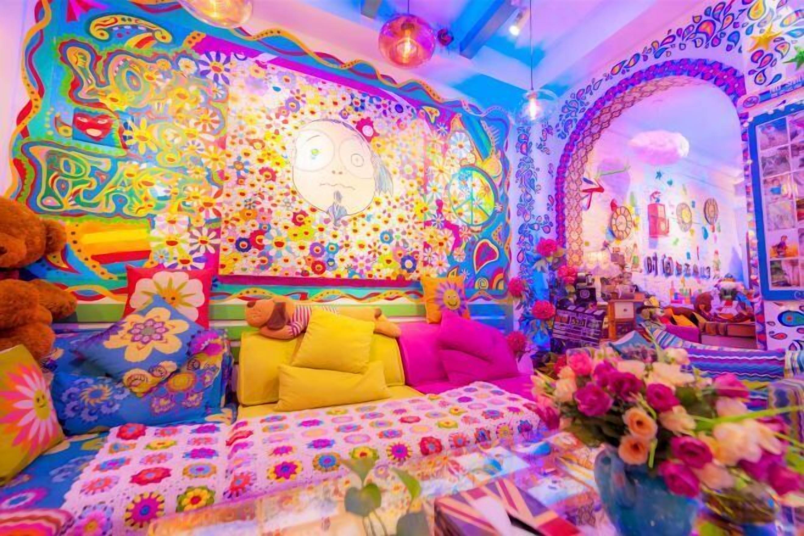 Um quarto vibrante com um edredom floral colorido, um urso de pelúcia grande e uma parede decorada com padrões psicodélicos e um relógio.