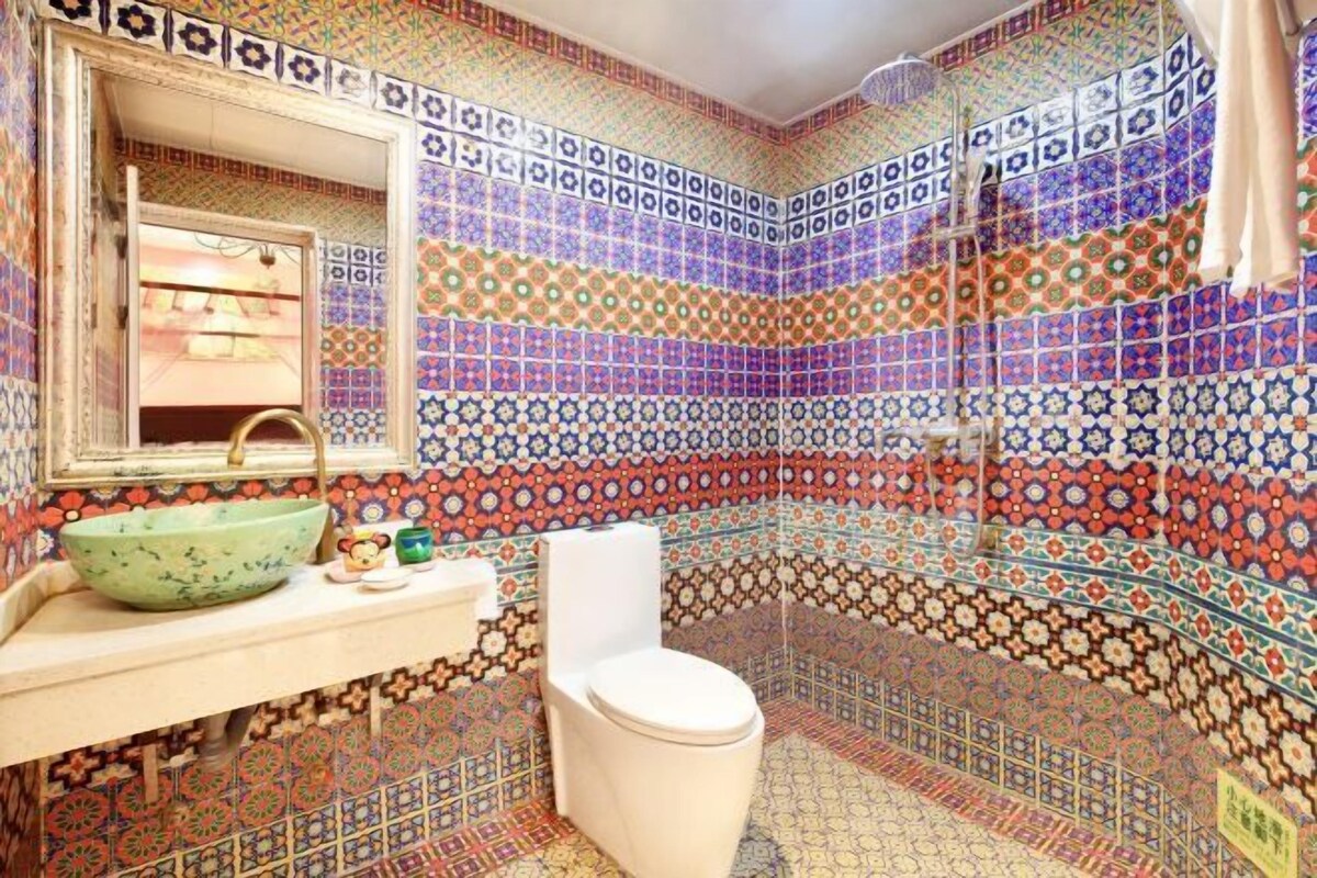 Un baño con baldosas de colores y diseños, un lavamanos con un lavabo verde y un inodoro blanco.