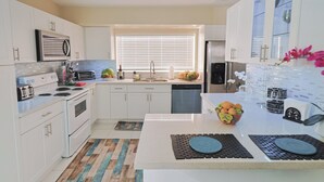 A modern kitchen with white cabinets, a stainless steel refrigerator, a built-in oven, and a large window with blinds. - Casa Bay-Spacious Family Friendly 4 Bedroom Home with Ultimate Backyard Fun! (Cutler Bay)
