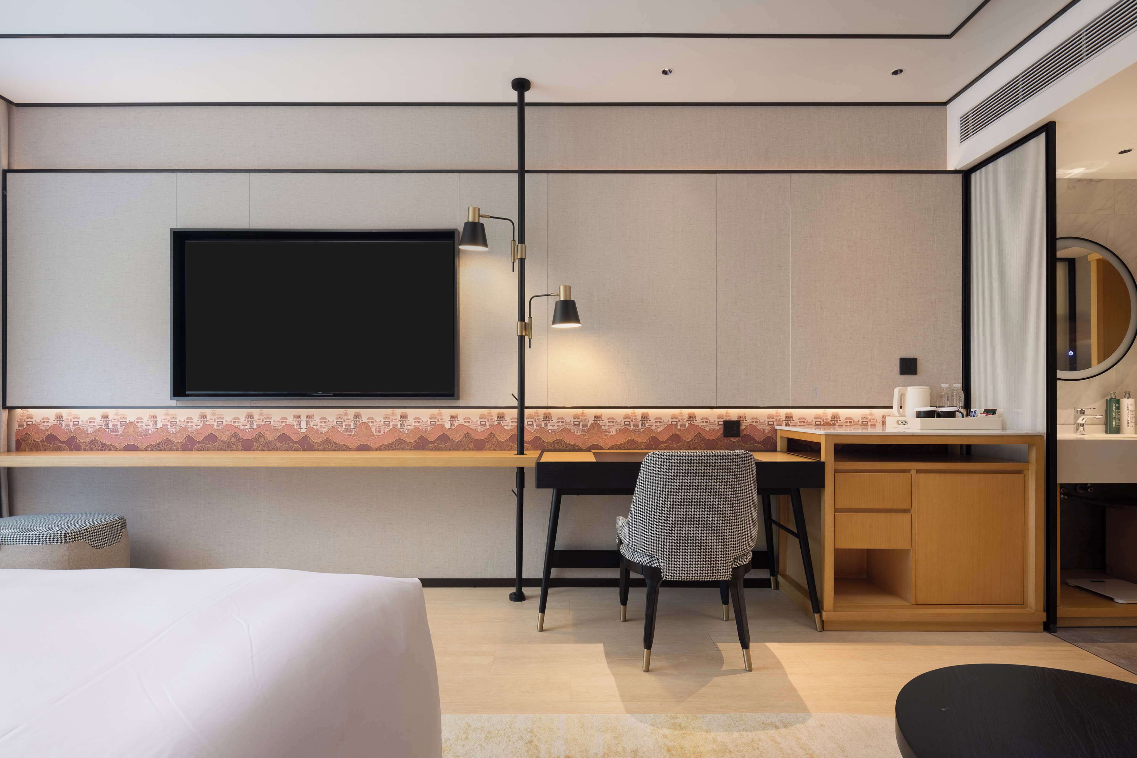 A hotel room with a bed, a desk with a chair, a television, and a small kitchenette.