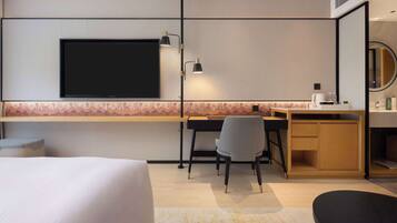Habitación de hotel con cama, escritorio con silla, televisor y una kitchenette pequeña.