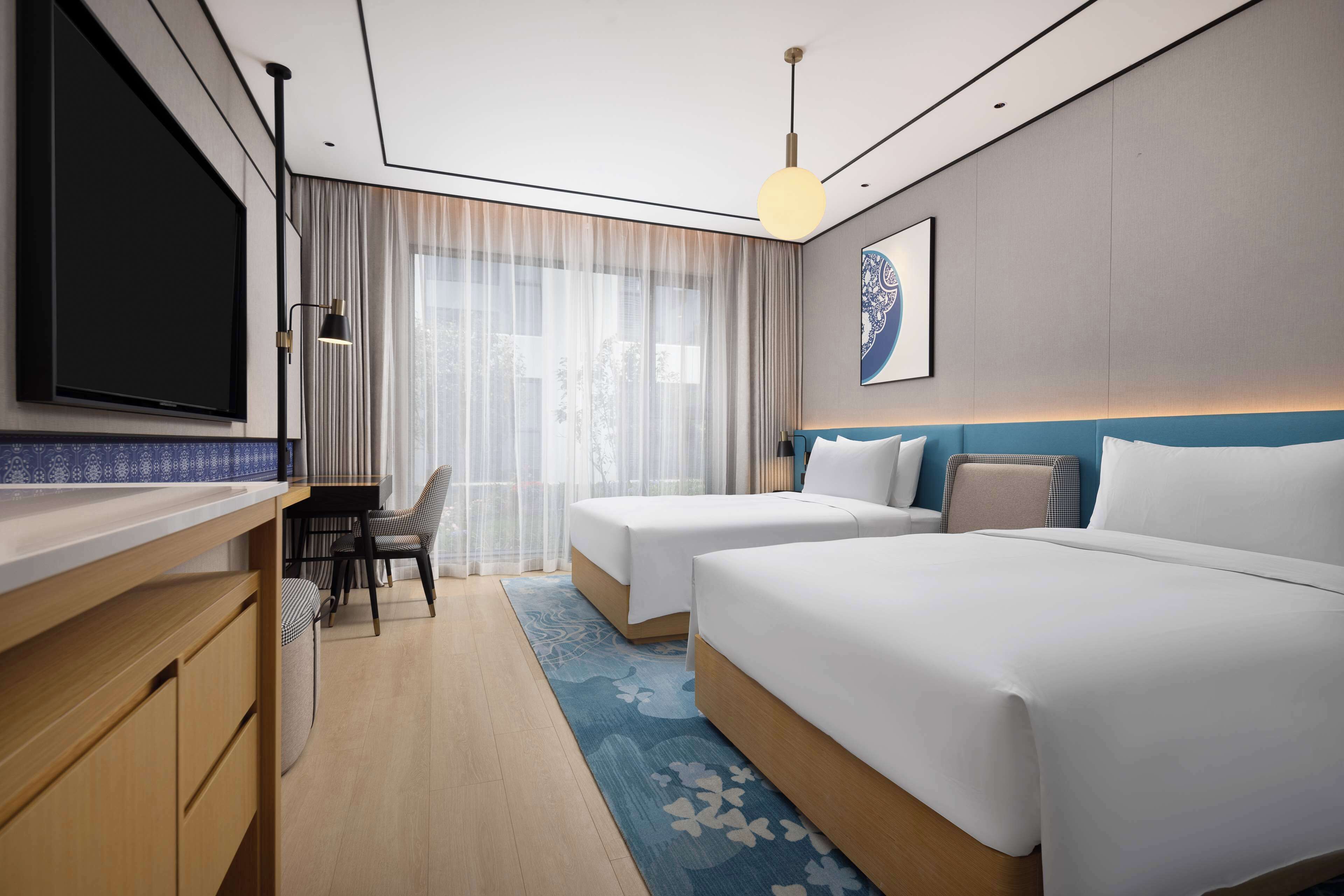 A modern hotel room with two beds, a desk, and a TV.