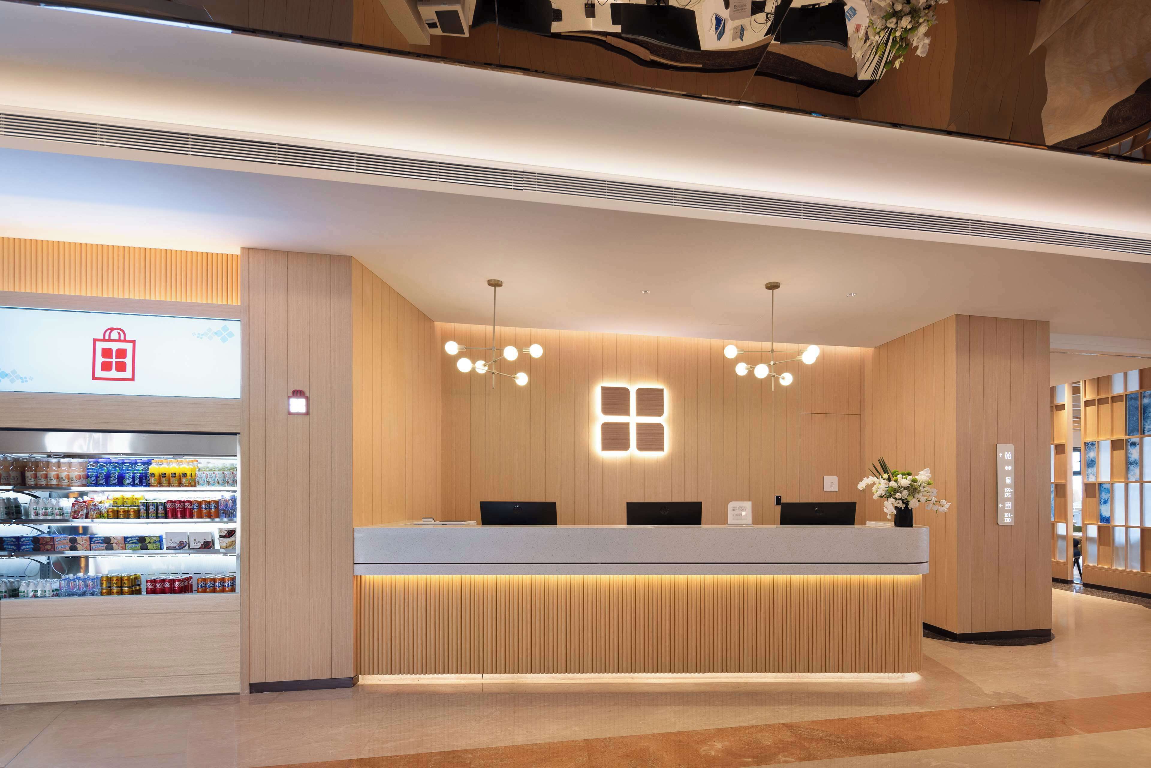 Una moderna recepción con encimera de madera, pantalla digital y enfriador de bebidas.